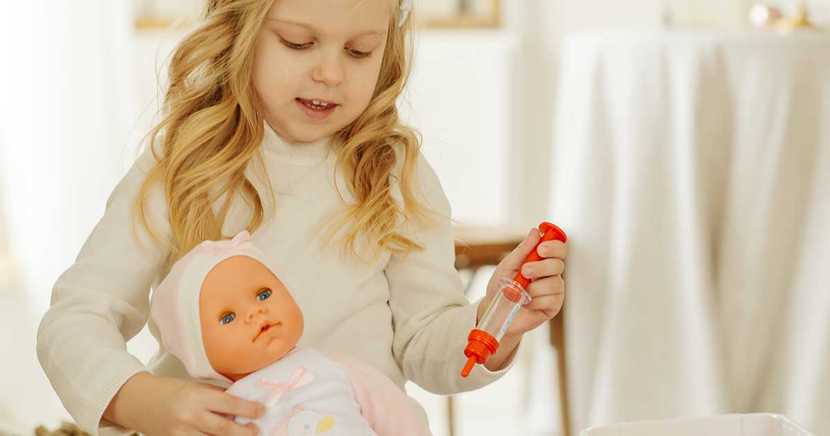 female child role-playing a doctor holding doll and a syringe