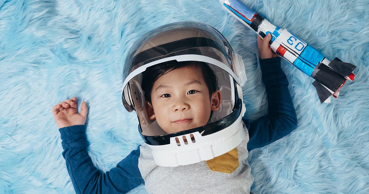 Asian boy wearing an astronaut helmet and holding a toy rocket