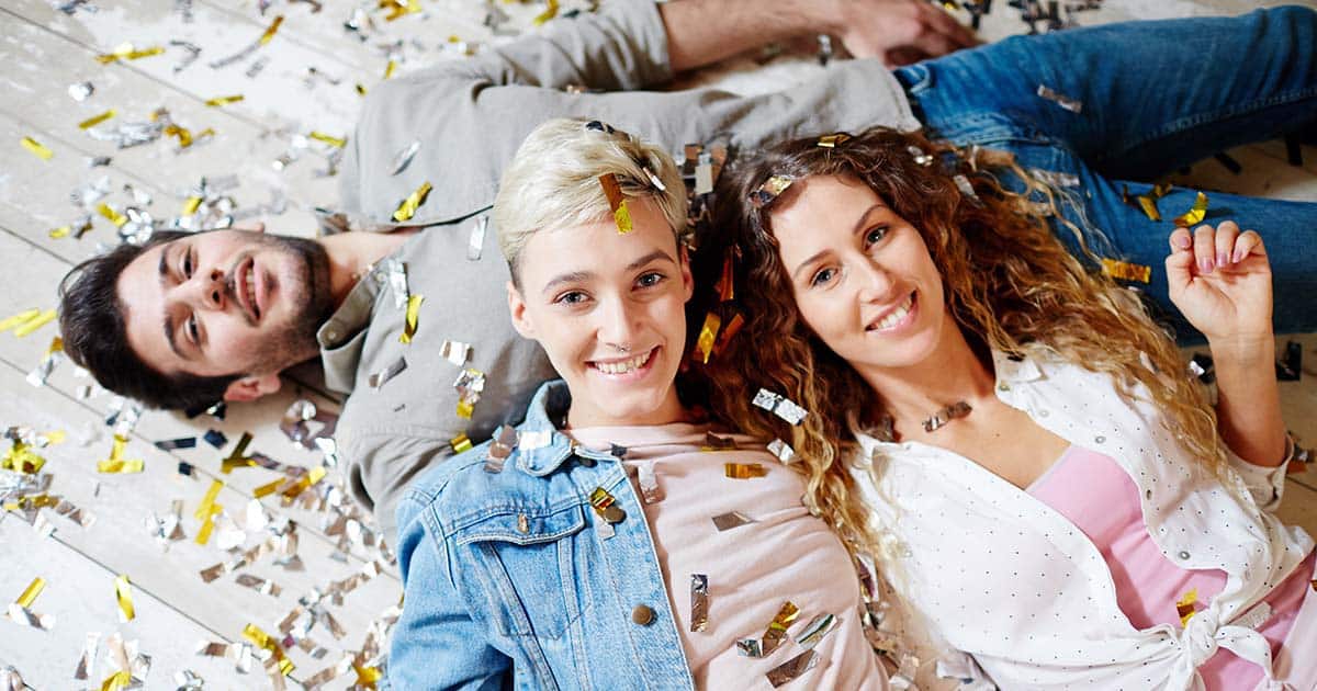 Two happy girls and guy lying on the floor after dance party in confetti
