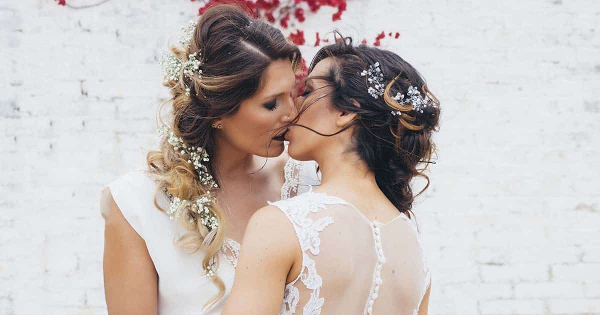lesbian couple kissing each other with white wedding dresses; same-sex marriage protected by Respect for Marriage Act