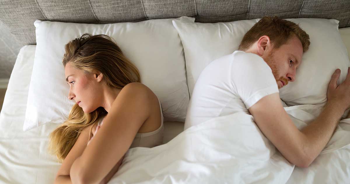 white couple in bed not facing each other looking upset
