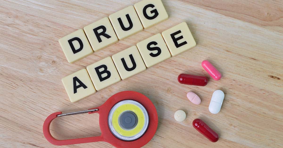 Top view of pill capsules, toy padlock and square letters with text DRUG ABUSE