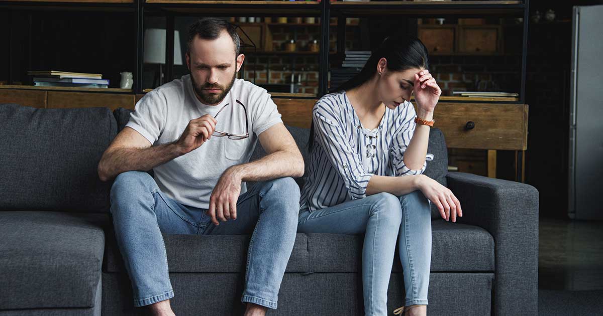 sad couple sitting on couch at home after quarrel and looking away